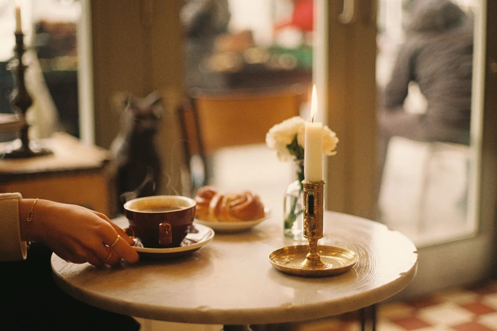 A cosy café table with coffee, a pastry and a lit candle